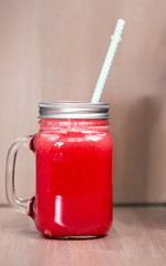 A watermelon smoothie in a mason jar with tube on wooden background
