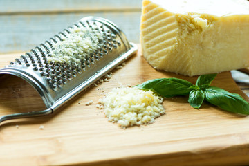 Heap of grated Parmesan on wooden background with leaf of basil