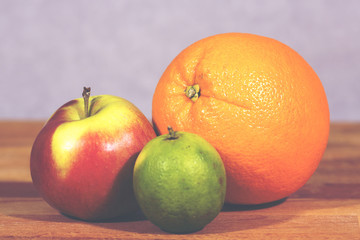 Fruits on a wooden table. The focus point is in the orange. Next to it there's an apple and a lime. Image has a vintage effect applied.
