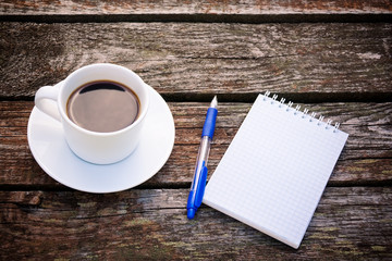 Coffee cup, notepad  and pen on wooden background
