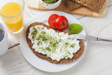 healthy spring summer low fat breakfast with orange juice,coffee,bread,cottage cheese, cress and tomatos at white wooden table