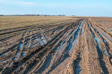Vanishing dirty road through fallow field with mud and puddles at early spring 
