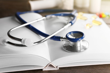 Stethoscope with open book and pills on wooden background. Medical literature concept