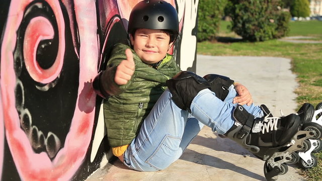 Portrait of a young skater with protective equipment  sitting against a wall and smiling to camera showing thumbs up