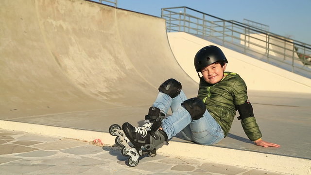 Young boy in frond  of a skating ramp sitting and smiling to camera showing thumbs up