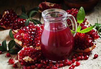 Jug with fresh pomegranate juice on the background of open grena