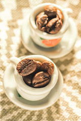 Coffee beans in a small lovely porcelain cups close-up. Strong coffee poster. Creative cozy design.
