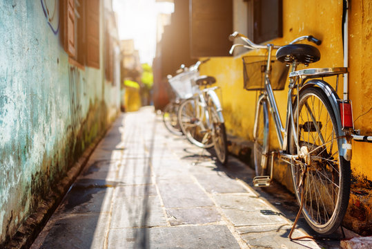 Bicycles Parked Near Yellow Wall Of Old House On Sunny Street