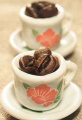 Coffee beans in a small lovely porcelain cups close-up. Strong coffee poster. Creative cozy design.
