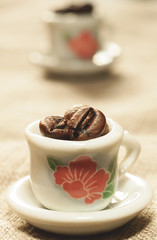 Coffee beans in a small lovely porcelain cups close-up. Strong coffee poster. Creative cozy design.
