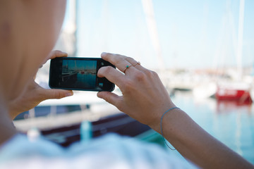 Young women shooting moored yacht on her smart-phone
