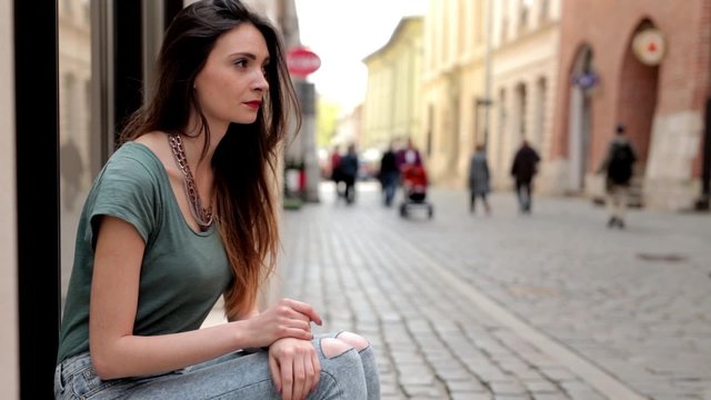Young brown hair girl sitting on the street and waiting for somebody, She is bored and angry