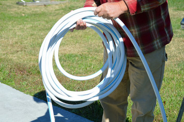 Man rolling the white hose of a camping trailer as he setups his campsite.