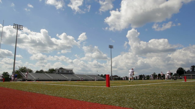 A punter practices on high school football stadium during mid day.