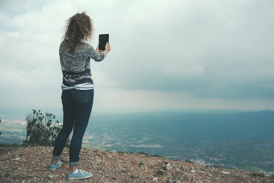 Young female tourist takes photos with smart phone on peak of rock