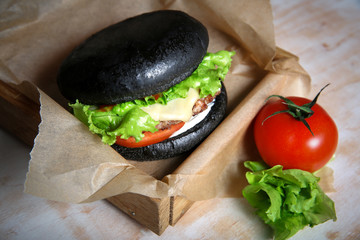 Black burger with vegeteables on wooden table