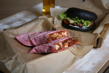Black burger with chicken pita and vegeteables on wooden table 