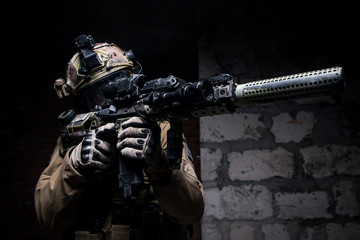 Soldier in military ammunition with gun/Man in military uniform and ammunition aiming from rifle on background of brick wall