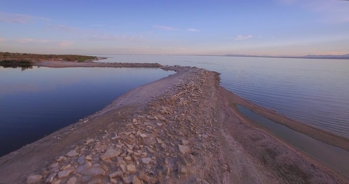 Fly By Rocky Bay / 4K flight above a rocky pier with bird flying closely ending clip over the water.