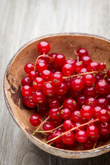 Redcurrant on a branch close to a wooden bowl.