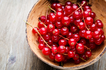 Redcurrant on a branch close to a wooden bowl.