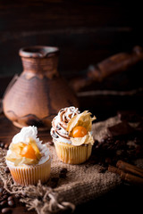 Chocolate cupcakes with white butter cream, decorated with winter cherry on a dark wooden background. Decorated with cinnamon sticks, coffee beans