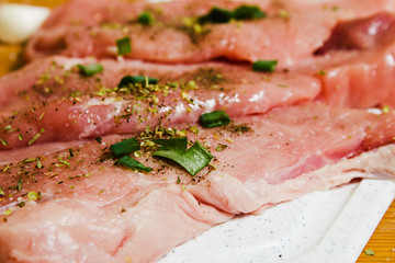 Sliced pork on a white board sprinkled with salt, Italian herbs and onion. Raw pork prepared to cook.