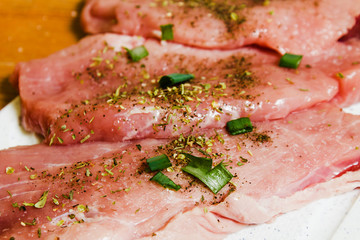 Sliced pork on a white board sprinkled with salt, Italian herbs and onion. Raw pork prepared to cook.