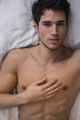 Shirtless sexy male model lying alone on his bed