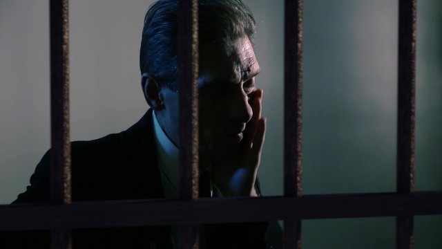 sad a grown man is behind bars in a prison cell