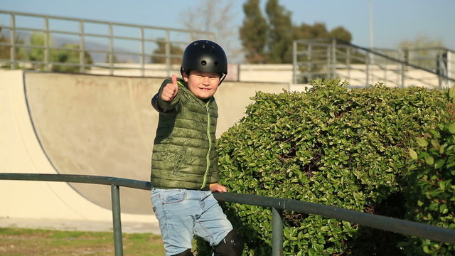 Young boy in frond  of a skating ramp standing and smiling to camera showing thumbs up