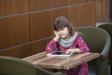 baby girl with tablet at a table in a cafe, waiting, shopping ce