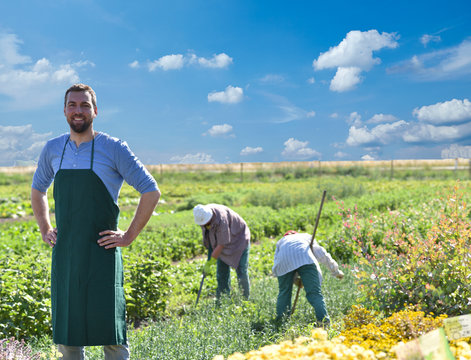 successful farmer on field in agriculture // Portrait eines Bauers am Feld, im hintergrund Arbeiter beim Ackerbau