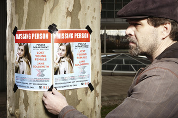 Police detective taping poster of missing person in city park