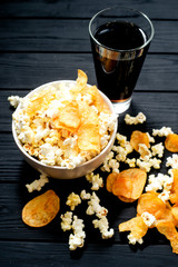 cheese popcorn in the bowl with a glass of cola or beer and potato chips on the wooden background