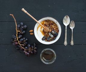 Healthy breakfast set. Bowl of oat granola with yogurt, fresh grapes, almond and  honey over black wooden backdrop