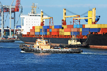 Fototapeta premium Tugboat assisting container cargo ship to harbor quayside