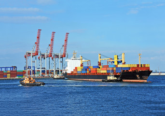 Tugboat assisting container cargo ship to harbor quayside
