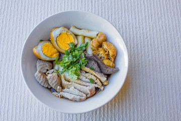 Chinese roll noodle soup with slice pork and  tofu, vegetables in a white ceramic bowl.
tradition food of thailand