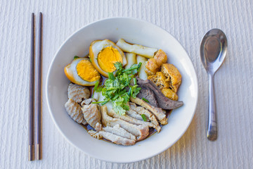 Chinese roll noodle soup with slice pork and  tofu, vegetables in a white ceramic bowl.
tradition food of thailand