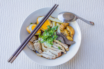 Chinese roll noodle soup with slice pork and  tofu, vegetables in a white ceramic bowl.
tradition food of thailand