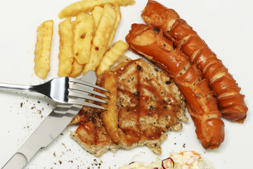 Pork steak and sausage with French fries on white dish.