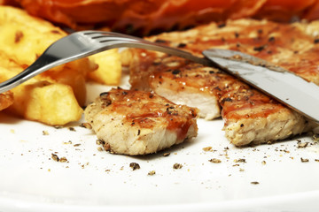 Pork steak and sausage with French fries on white dish.