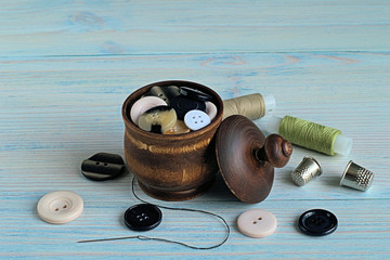  Sewing accessories.   Buttons for clothes in a wooden pot and coils of sewing threads on a blue...