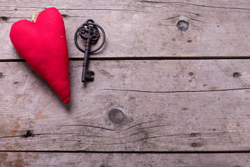 Decorative  heart and vintage key on aged wooden background.