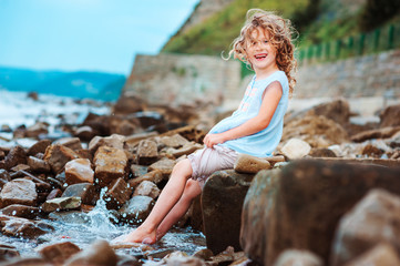 funny child girl playing with water splash on the beach. Traveling on summer vacation. Happy childhood concept.