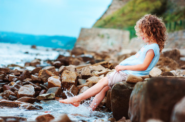 funny child girl playing with water splash on the beach. Traveling on summer vacation. Happy childhood concept.