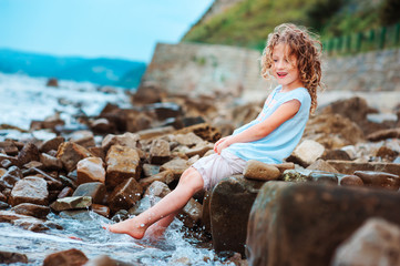 funny child girl playing with water splash on the beach. Traveling on summer vacation. Happy childhood concept.