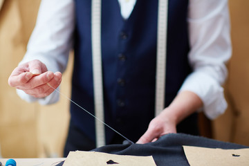 Hands of tailor with needle and thread sewing clothes