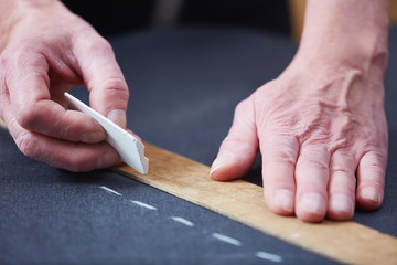 Hands of tailor dotting with chalk on textile